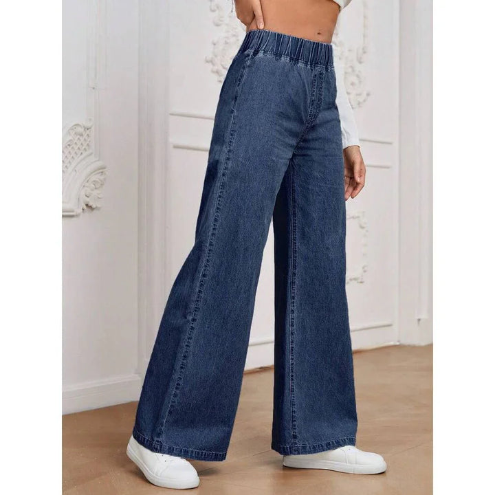 Woman wearing dark blue high-waisted wide-leg denim jeans and white sneakers indoors