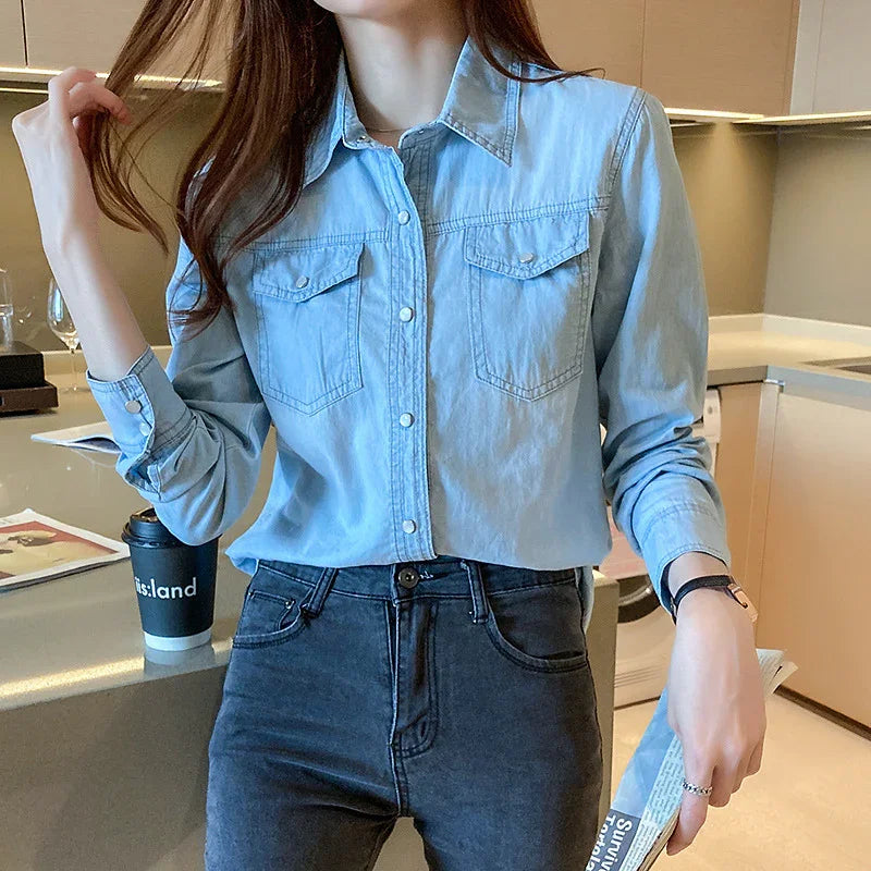 Woman wearing light blue denim button-up shirt with chest pockets and dark jeans in modern kitchen
