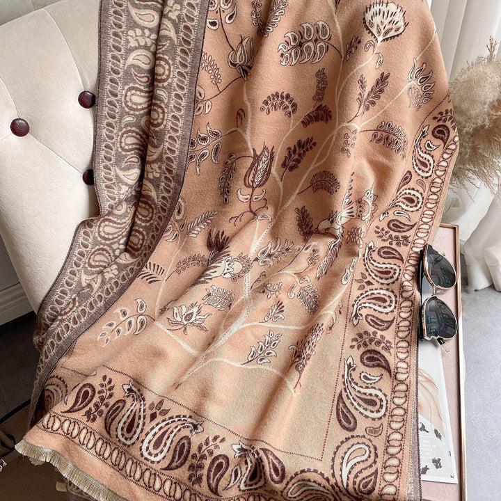 Beige and brown floral patterned throw blanket draped over cream tufted chair with sunglasses on side table