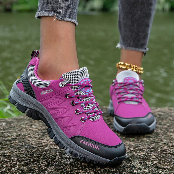 Close-up of pink and black outdoor hiking shoes with gray soles worn with rolled-up jeans near water