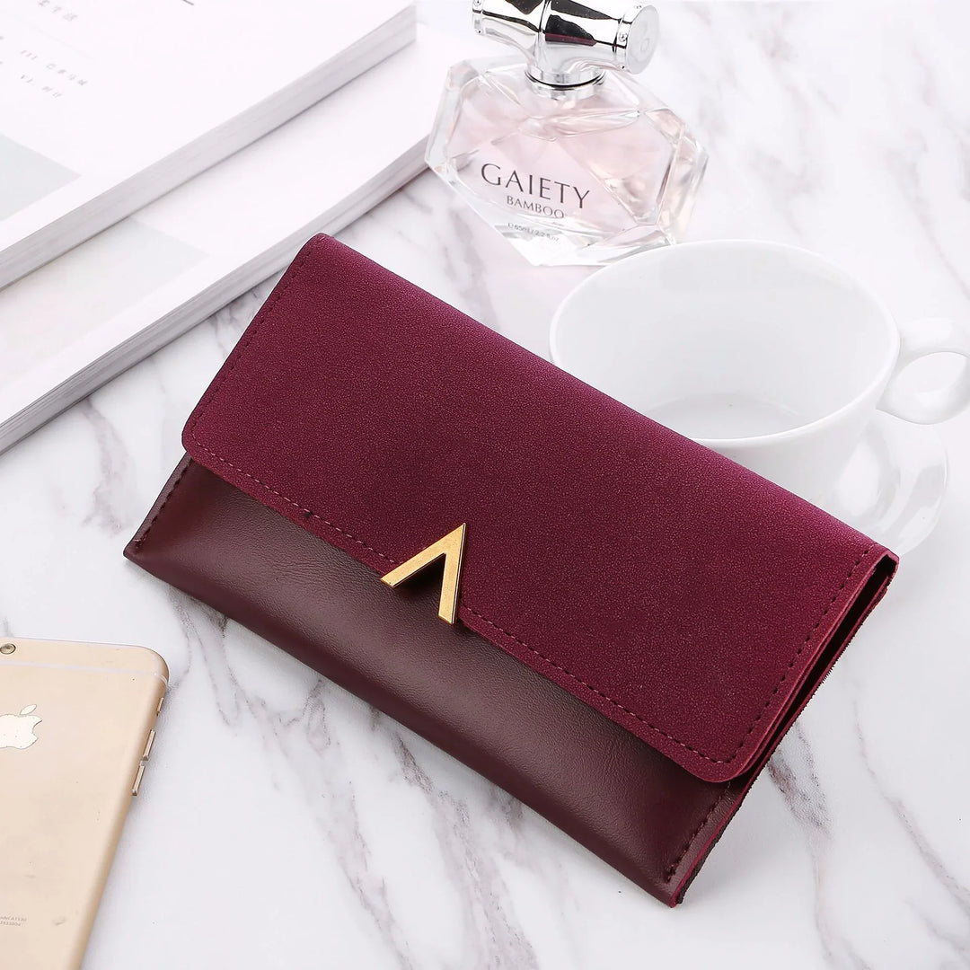 Burgundy two-tone leather wallet with gold V detail on white marble table with perfume bottle, cup, and phone