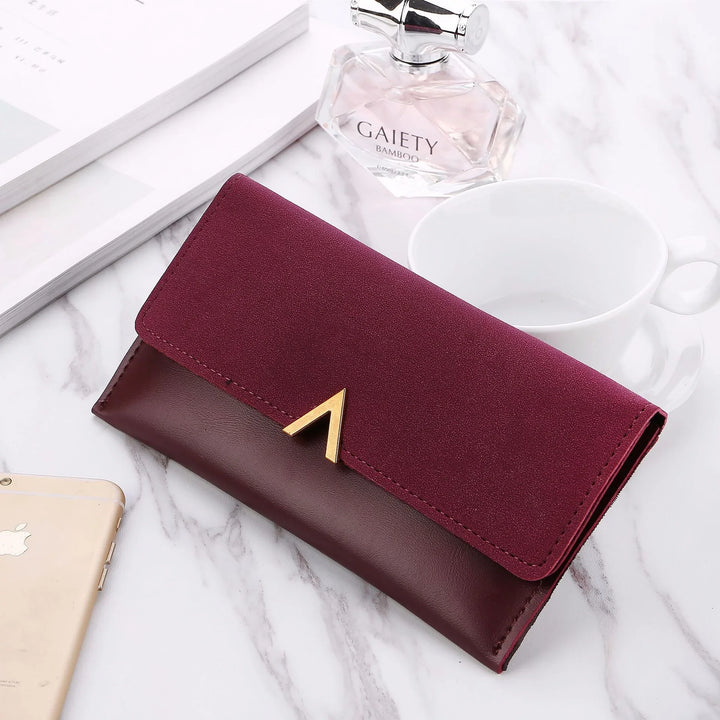 Burgundy two-tone leather wallet with gold V detail on white marble table with perfume bottle, cup, and phone