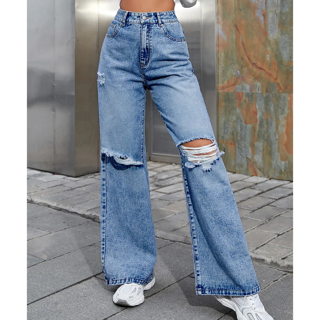 Woman wearing high-waisted ripped wide-leg blue jeans with white sneakers on urban pavement