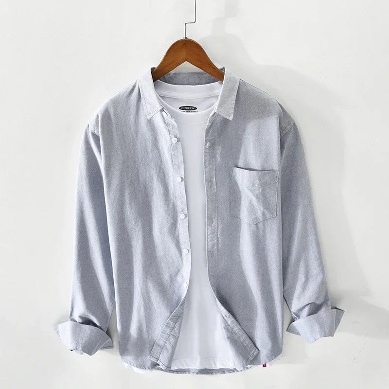 Light grey button-up shirt layered over a white T-shirt on wooden hanger against white wall