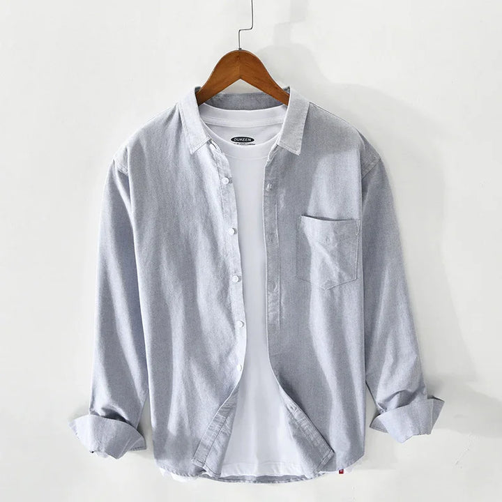 Light grey button-up shirt layered over a white T-shirt on wooden hanger against white wall