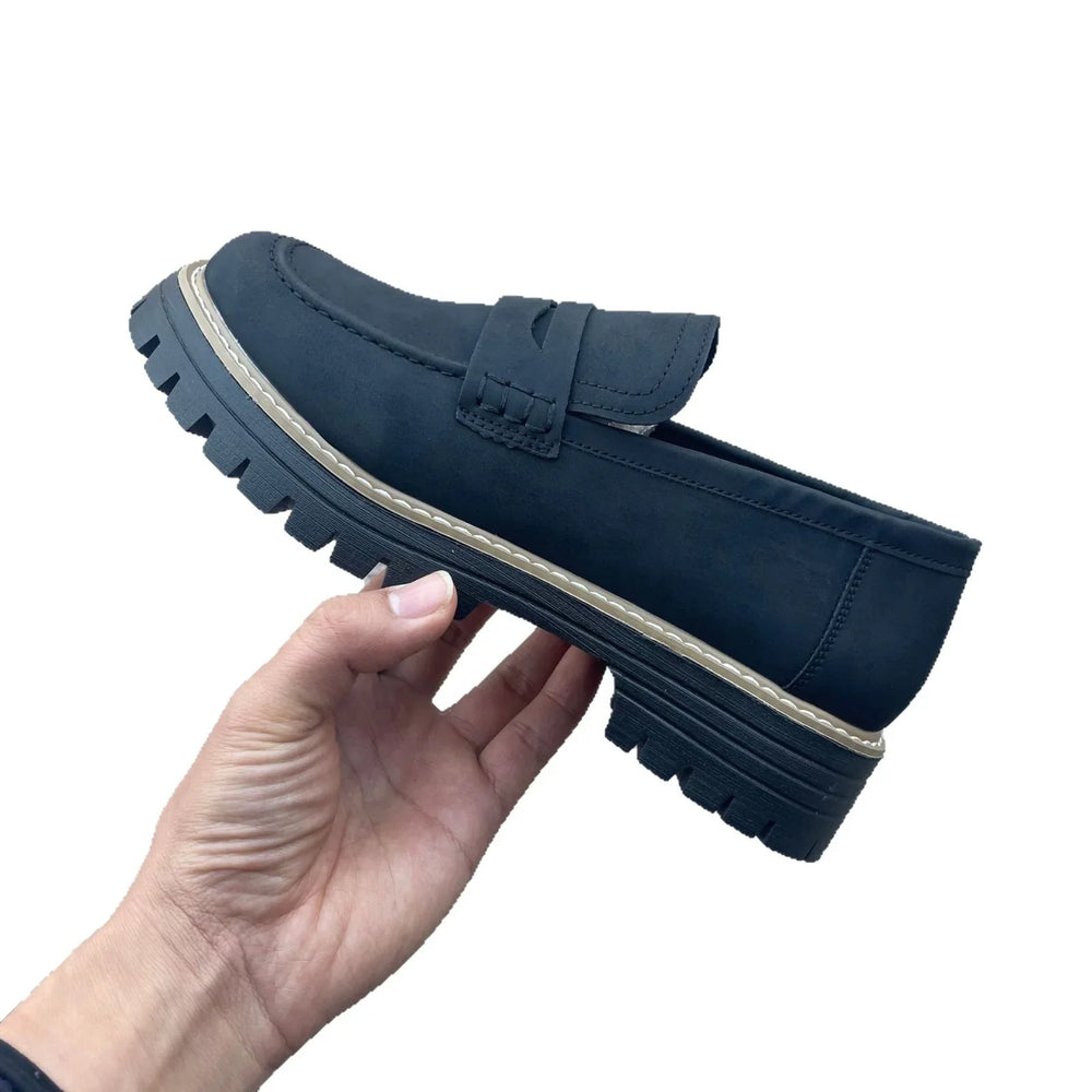 Hand holding black chunky sole loafer shoe with beige trim on white background