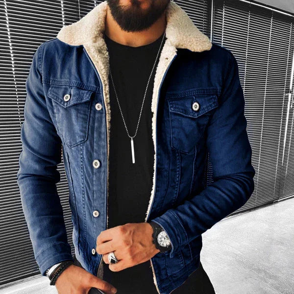 Man wearing dark blue sherpa-lined denim jacket with black shirt, silver necklace, wristwatch, and rings