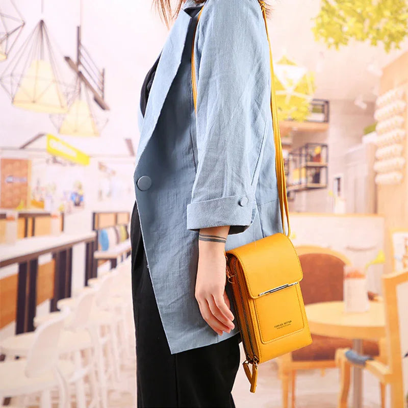 Woman wearing light blue blazer and black pants holding a yellow crossbody bag in café
