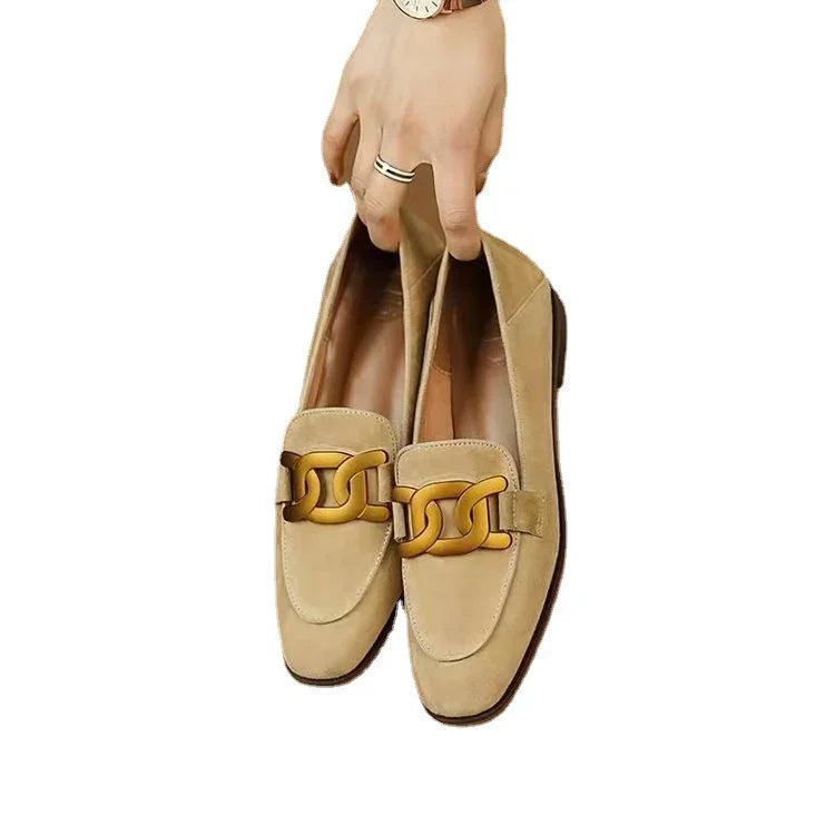 Hand holding beige suede loafers with large gold chain detail on white background