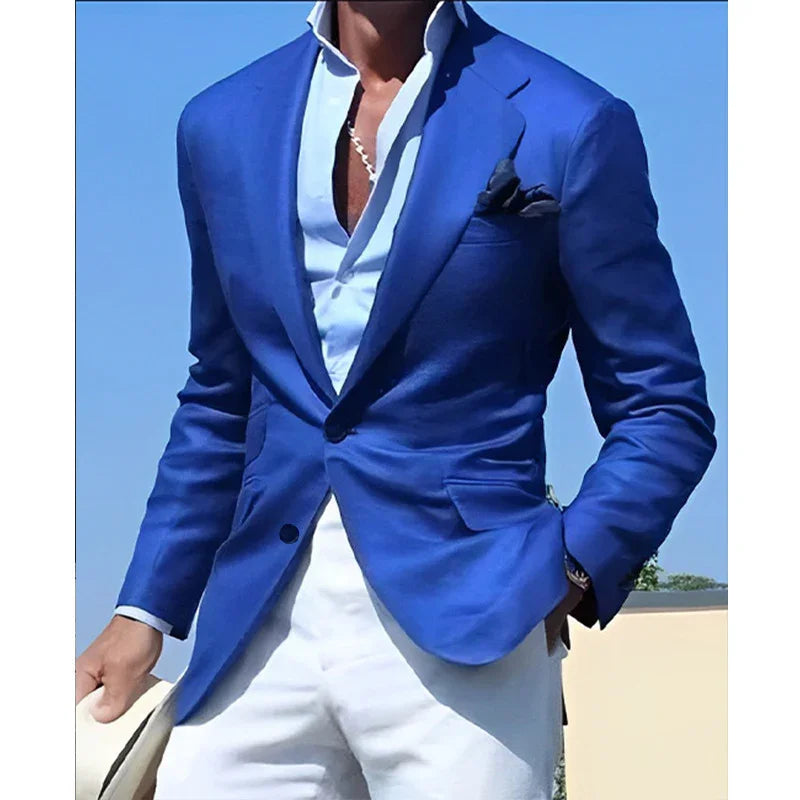 Man wearing a fitted royal blue blazer, white shirt, white pants, and a chain necklace outdoors