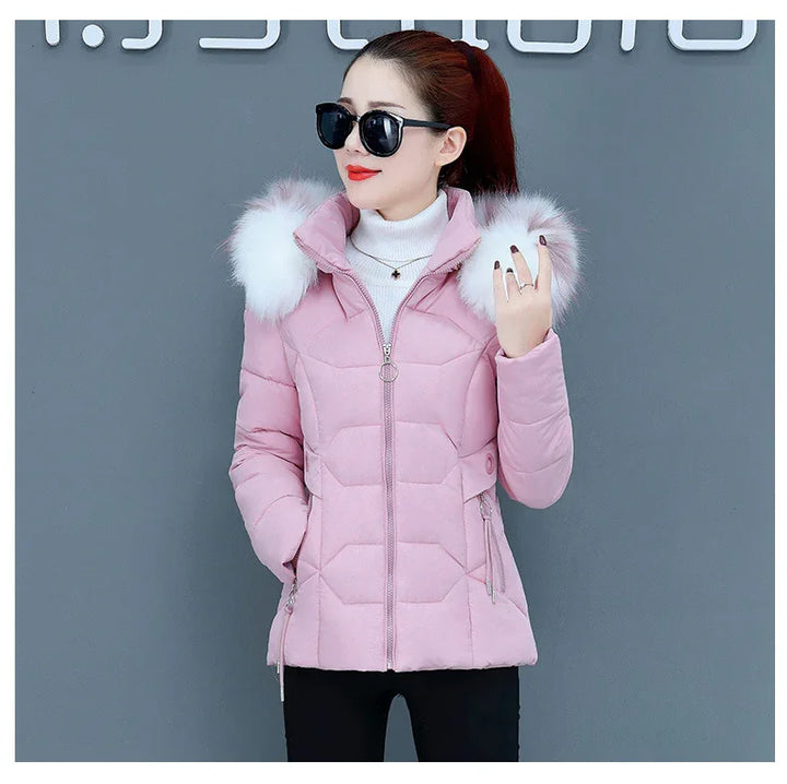 Woman wearing a pink quilted winter jacket with white faux fur hood and black sunglasses