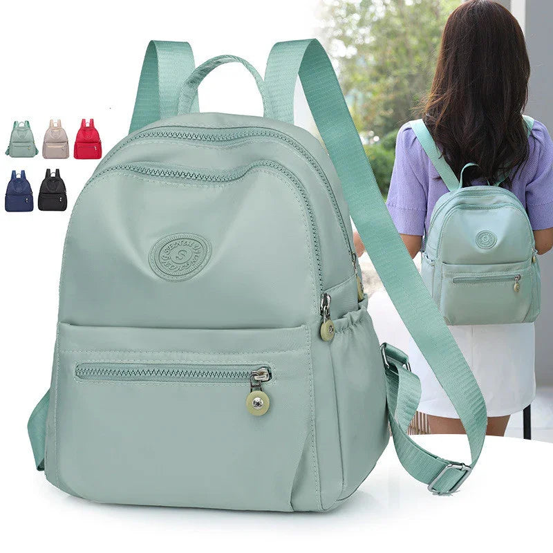 Mint green small backpack with multiple zippered compartments and adjustable straps, shown worn by a woman
