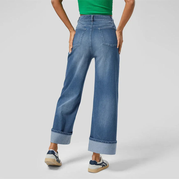 Rear view of person wearing high-waisted wide-leg blue jeans with cuffed hems and sneakers