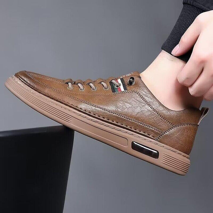 Brown leather casual sneaker with rubber sole and lace-up design on foot against gray background