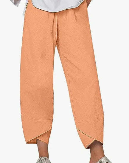 Orange cropped pants with unique angled hems worn with casual shoes on white background