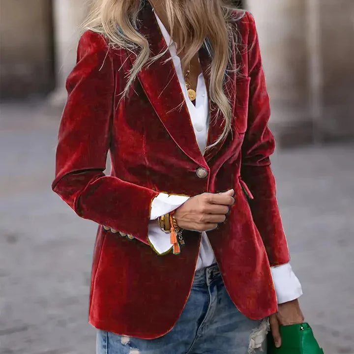 Woman wearing a red velvet blazer over white shirt and distressed jeans, holding green clutch