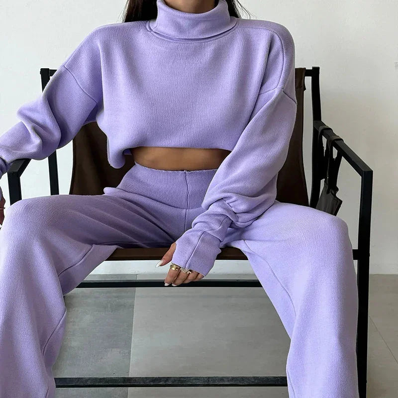 Woman in lavender cropped turtleneck sweater and matching wide-leg pants sitting on a modern chair
