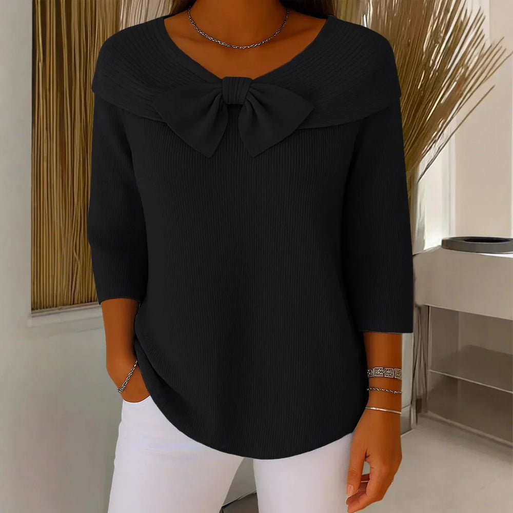 Woman wearing black ribbed knit top with large bow detail and 3/4 sleeves, paired with white pants