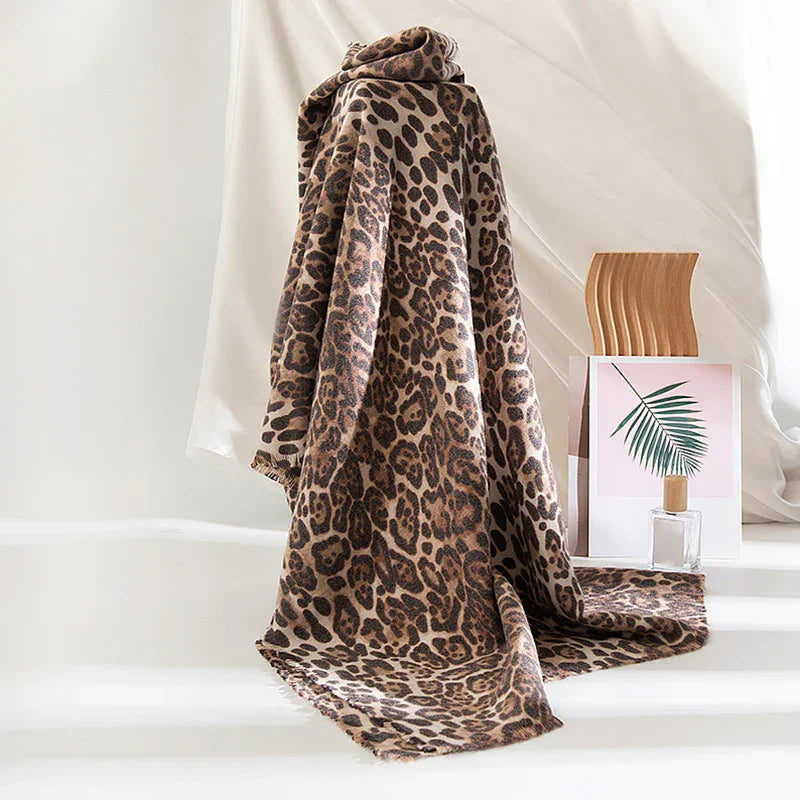 Leopard print soft scarf draped on white surface with wooden decor and framed leaf art