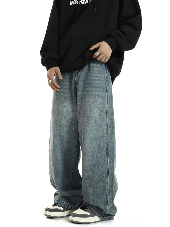 Person wearing oversized baggy blue jeans, black hoodie, and black white sneakers with silver rings