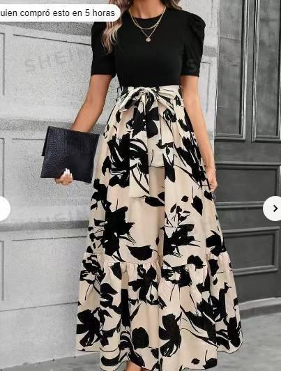 Woman wearing black puff sleeve top with long beige skirt featuring large black floral print, holding black clutch