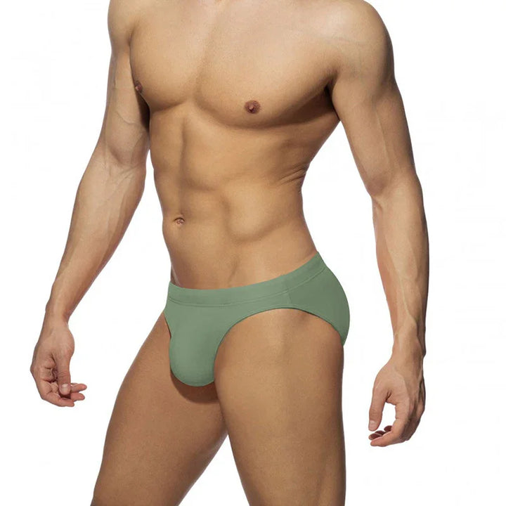 Muscular male model wearing green low-rise briefs on white background