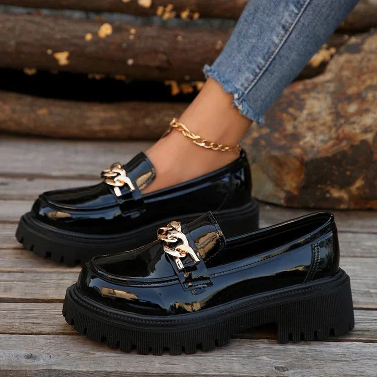 Black patent leather chunky sole loafers with gold chain detail worn with blue jeans and gold ankle bracelet