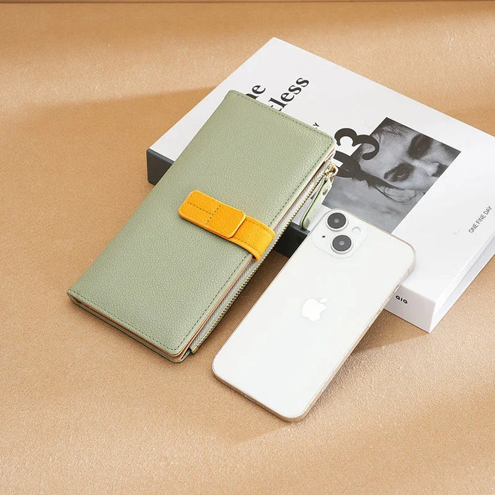 Light green wallet with yellow strap, white iPhone, and a black and white book on beige surface