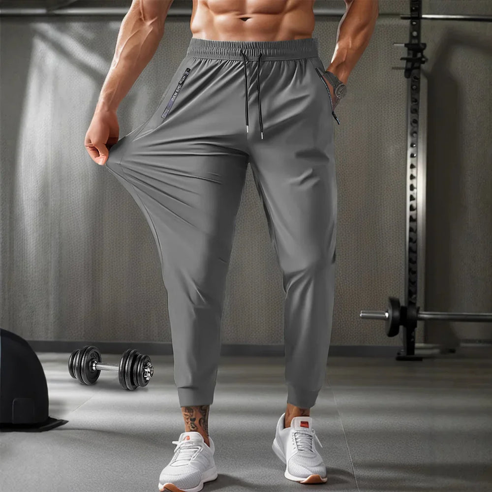 Man wearing stretchy gray workout joggers in gym with dumbbells and gym equipment