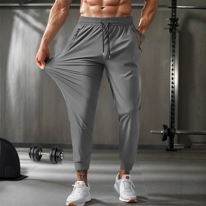 Man wearing stretchy gray workout joggers in gym with dumbbells and gym equipment