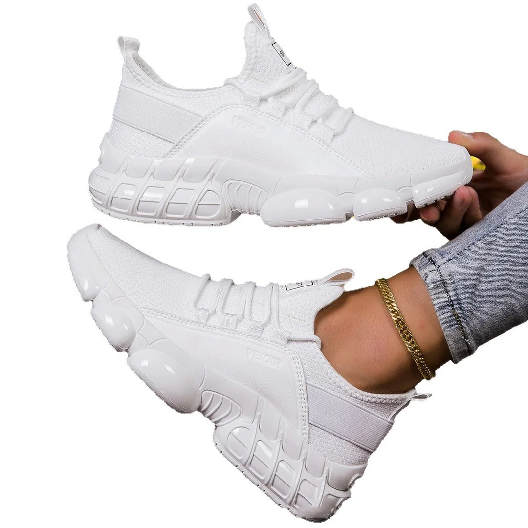 Pair of white modern sporty sneakers with textured soles, worn with jeans and gold ankle bracelet