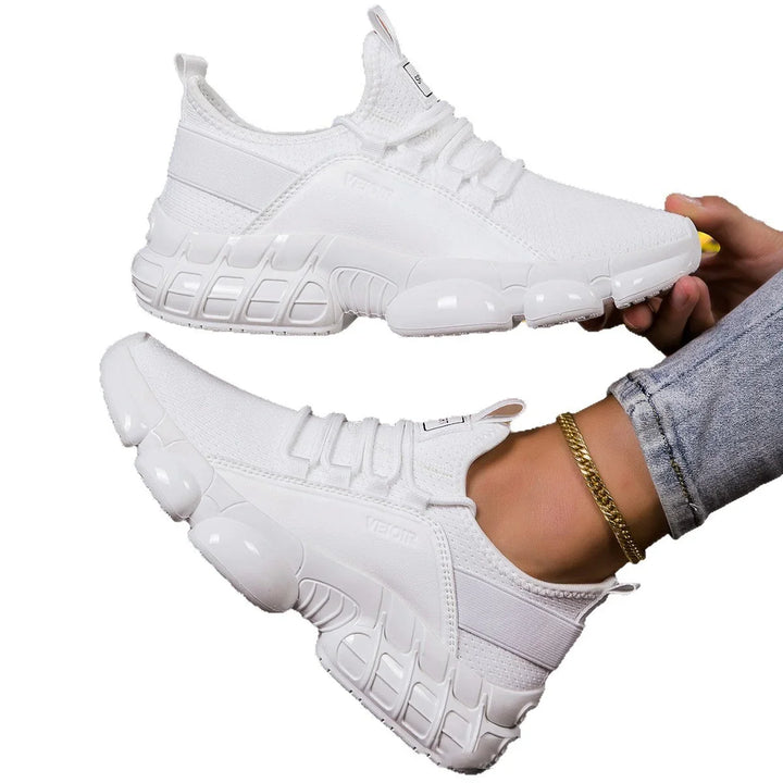 Pair of white modern sporty sneakers with textured soles, worn with jeans and gold ankle bracelet