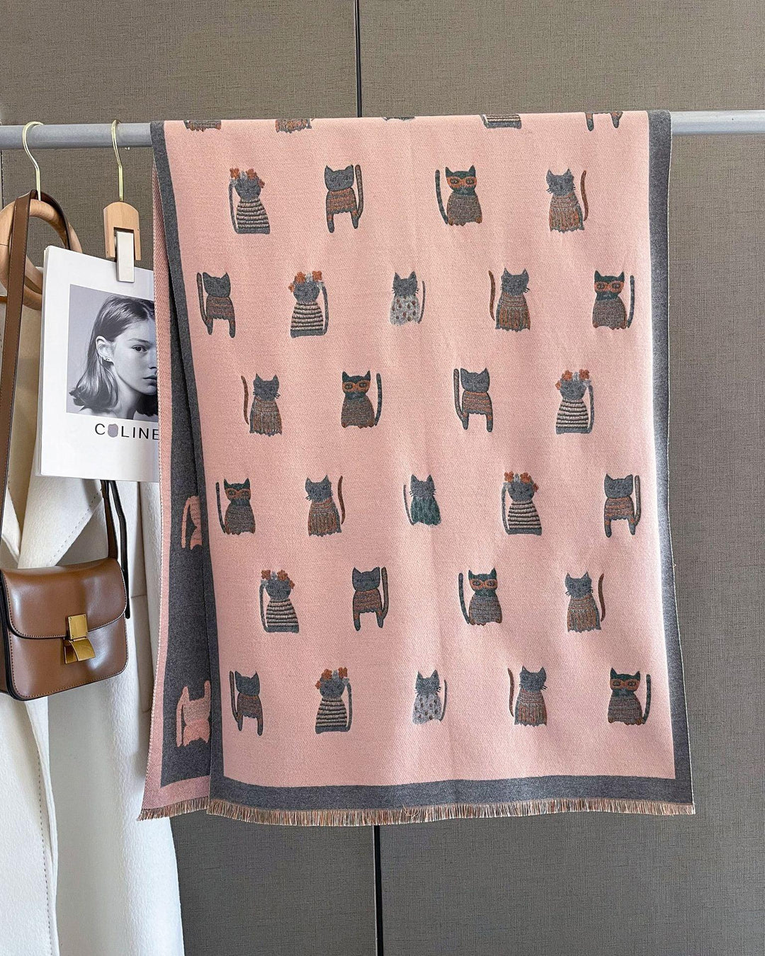 Pink scarf with cute cat patterns hanging on a rack with a brown purse and white coat