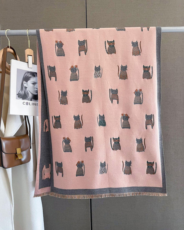 Pink scarf with cute cat patterns hanging on a rack with a brown purse and white coat