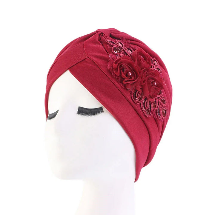 Red fabric turban hat with decorative floral appliqué and beads on white mannequin head