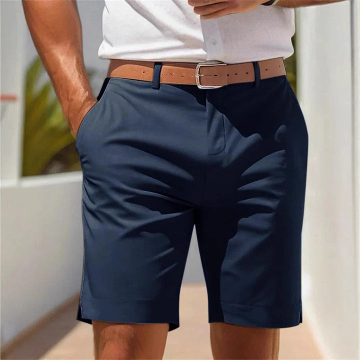 Man wearing navy blue shorts with brown belt and white shirt outdoors in bright sunlight