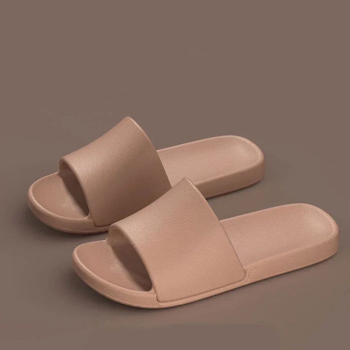 Beige unisex slide sandals with textured strap and footbed on brown background
