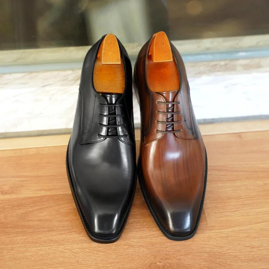 Pair of polished men's leather dress shoes in black and brown on wooden floor