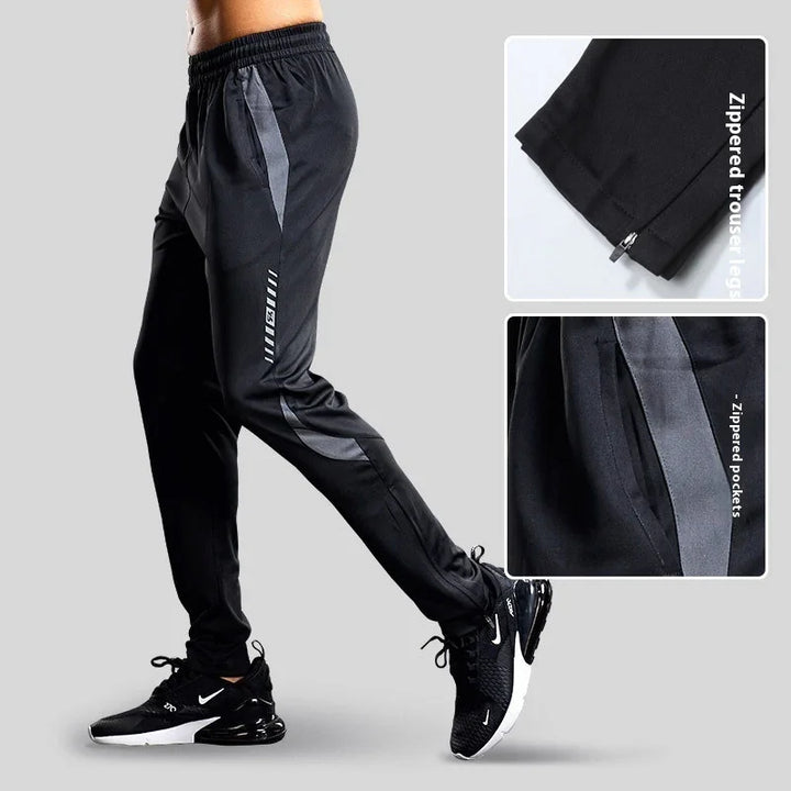 Black sporty track pants with gray stripes, zippered trouser legs, zippered pockets, worn with black Nike sneakers