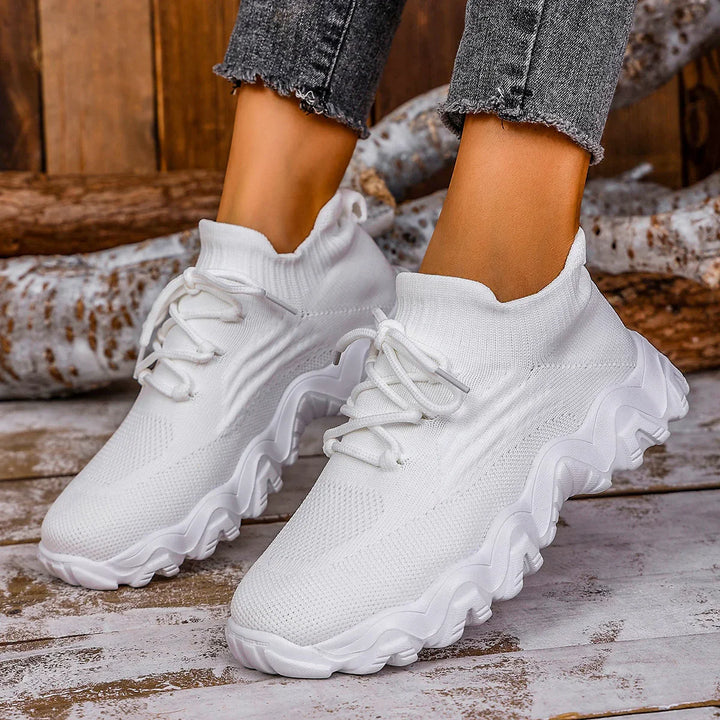 Trendy white knit sock sneakers with chunky wavy sole worn with frayed hem jeans on wooden floor