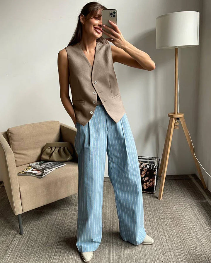 Woman taking selfie wearing brown sleeveless vest and blue pinstripe wide-leg pants in modern room
