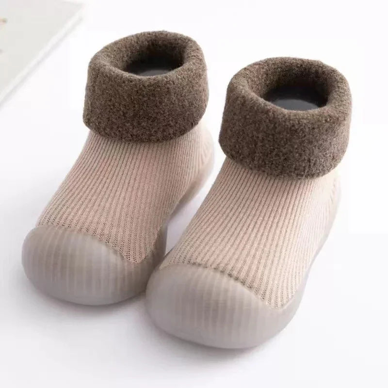 Beige knit baby shoes with soft brown fuzzy cuffs and flexible rubber soles on white background