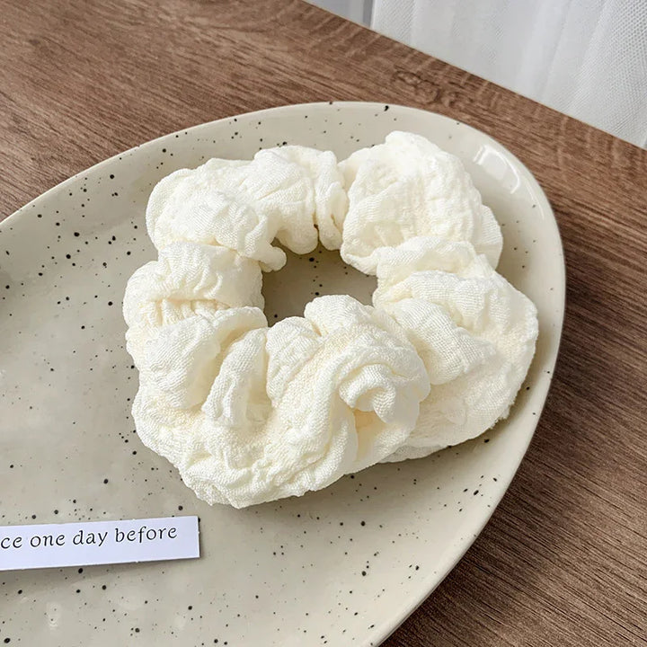 Cream-colored soft fabric scrunchie on a speckled ceramic plate on wooden table