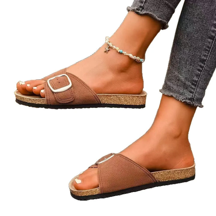 Close-up of feet in brown slide sandals with buckle and anklet, paired with frayed black jeans