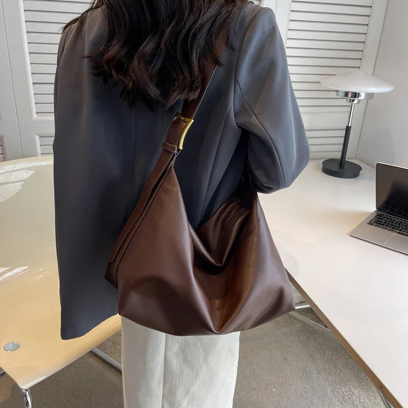 Woman wearing gray blazer and white pants carrying large brown leather shoulder bag in office setting