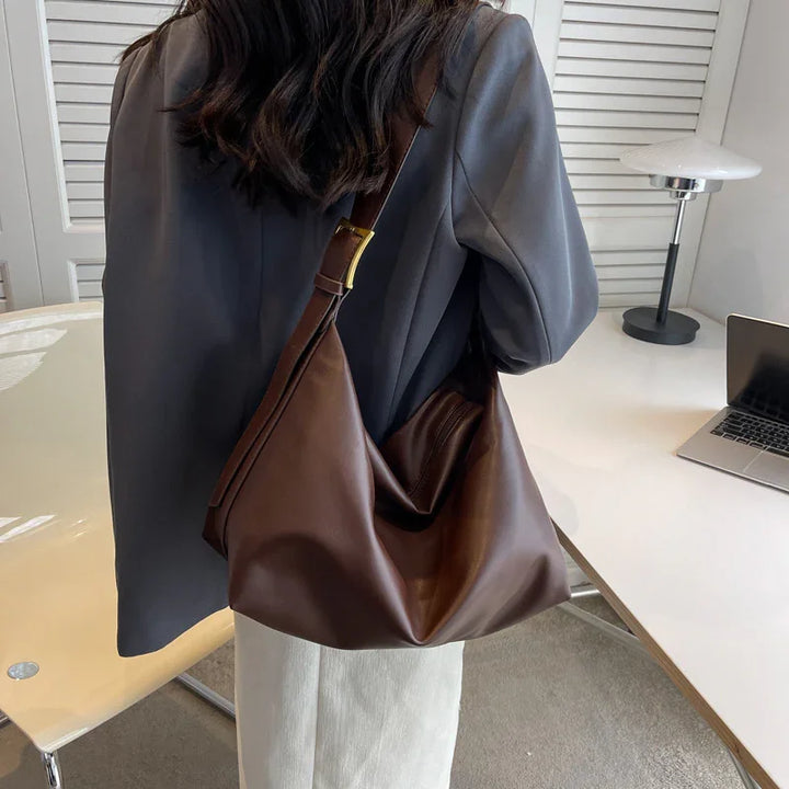Woman wearing gray blazer and white pants carrying large brown leather shoulder bag in office setting