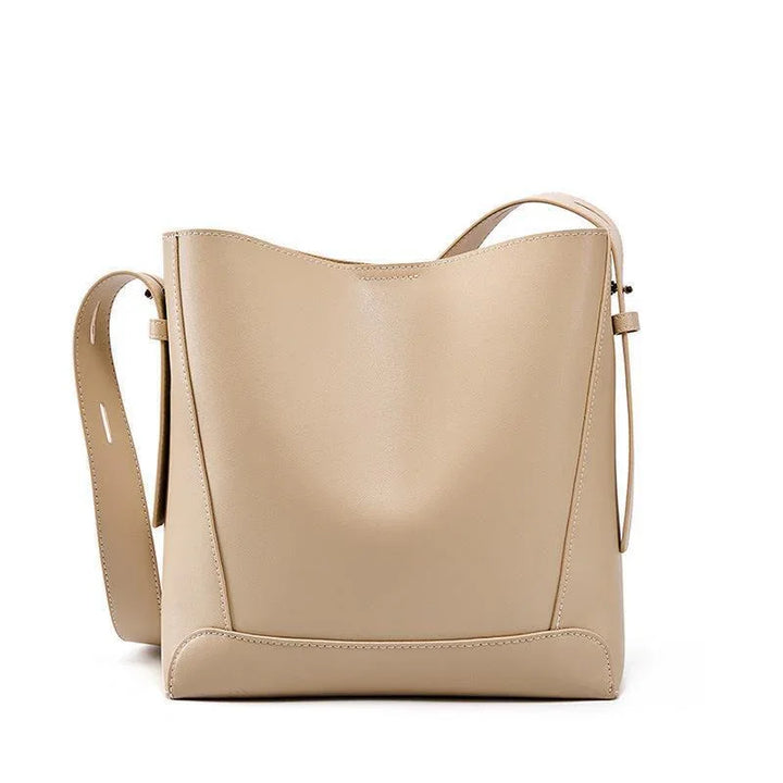 Minimalist beige leather bucket bag with adjustable shoulder strap on white background