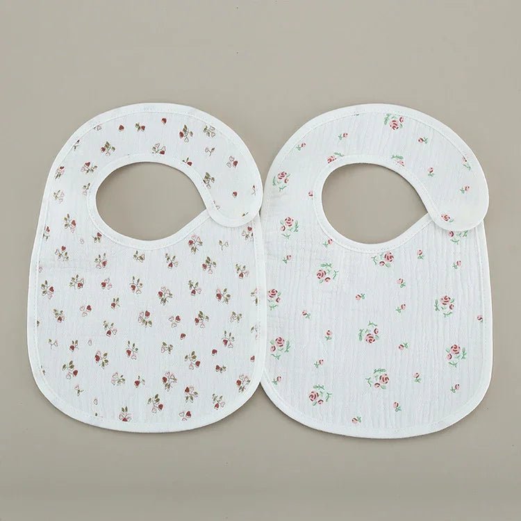 Two white baby bibs with small floral prints laid flat on a beige background