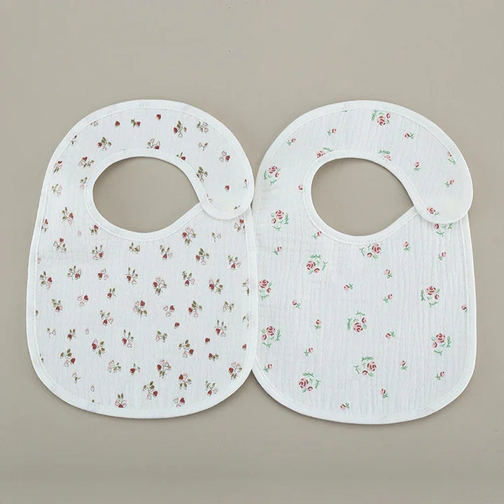 Two white baby bibs with small floral prints laid flat on a beige background