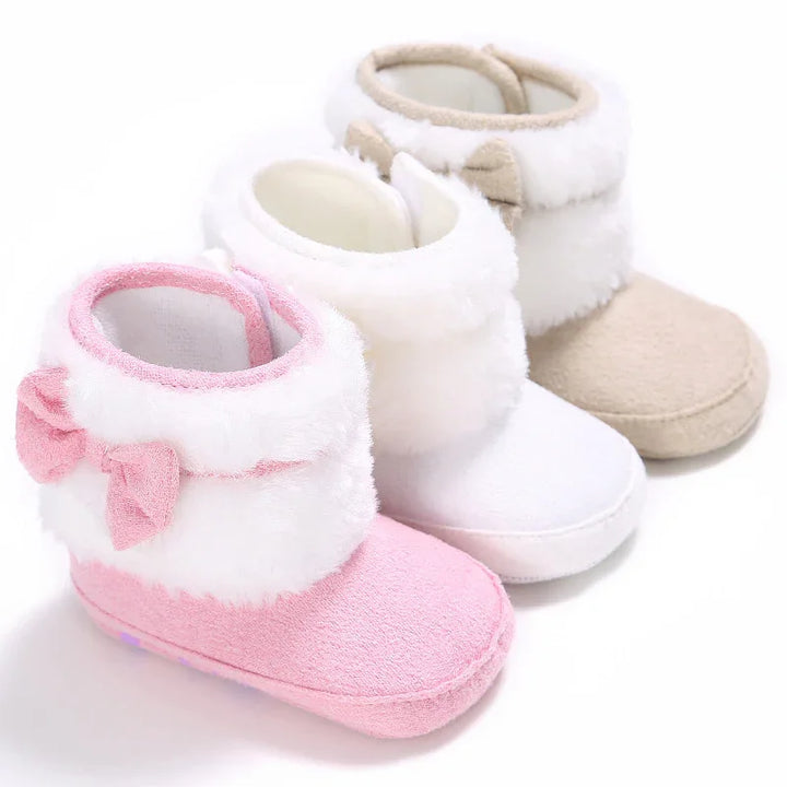 Three soft baby booties in pink, white, and beige with fluffy cuffs and bow details